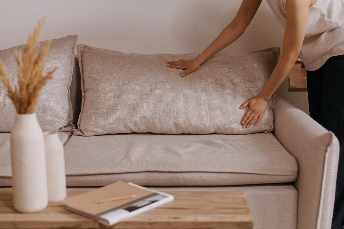 A person arranging the pillows of a sofa
