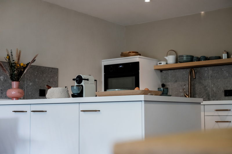 Helle Küchenzeile mit Backofen, Kaffeemaschine und Holzarbeitsfläche im Apartment von Hugo & Pepi.