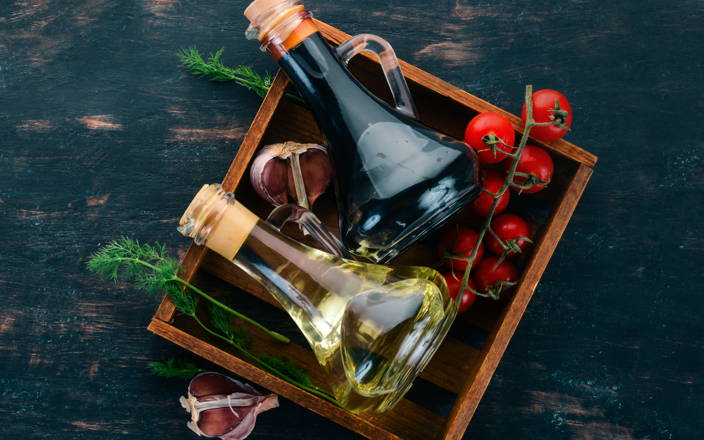 A square wooden tray with oils, vinegars, tomatoes, dill & garlic on it.