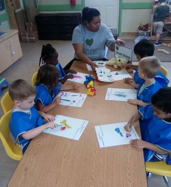 Teacher sitting down with children using paint and looking at different plastic toys