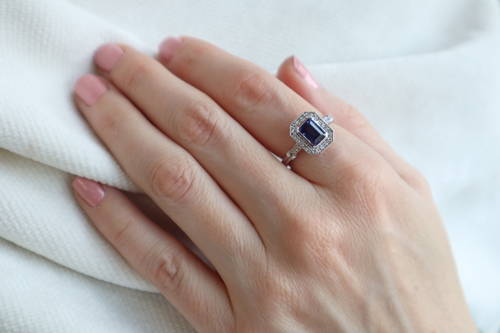 Une main déposée sur un vêtement blanc porte une bague avec saphir et diamants à l'index.
