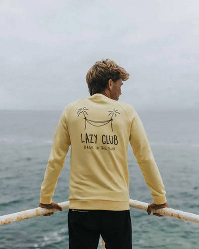 Man standing facing the sea with a yellow organic cotton sweatshirt with palm tree illustration printed on the reverse