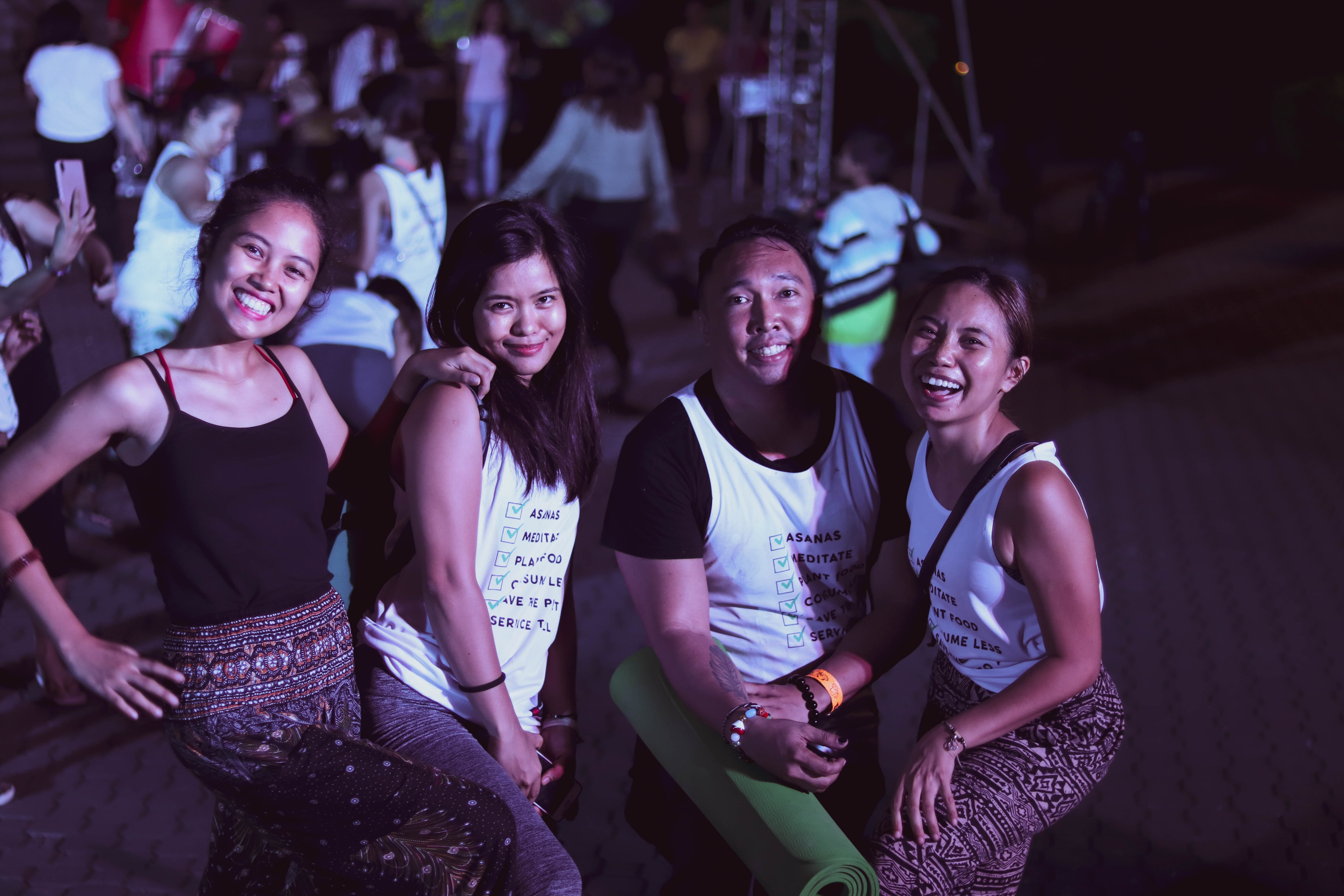 image of 4 young asian women posing for the camera together smiling and laughing. they are at a concert at nighttime and are under a light.
