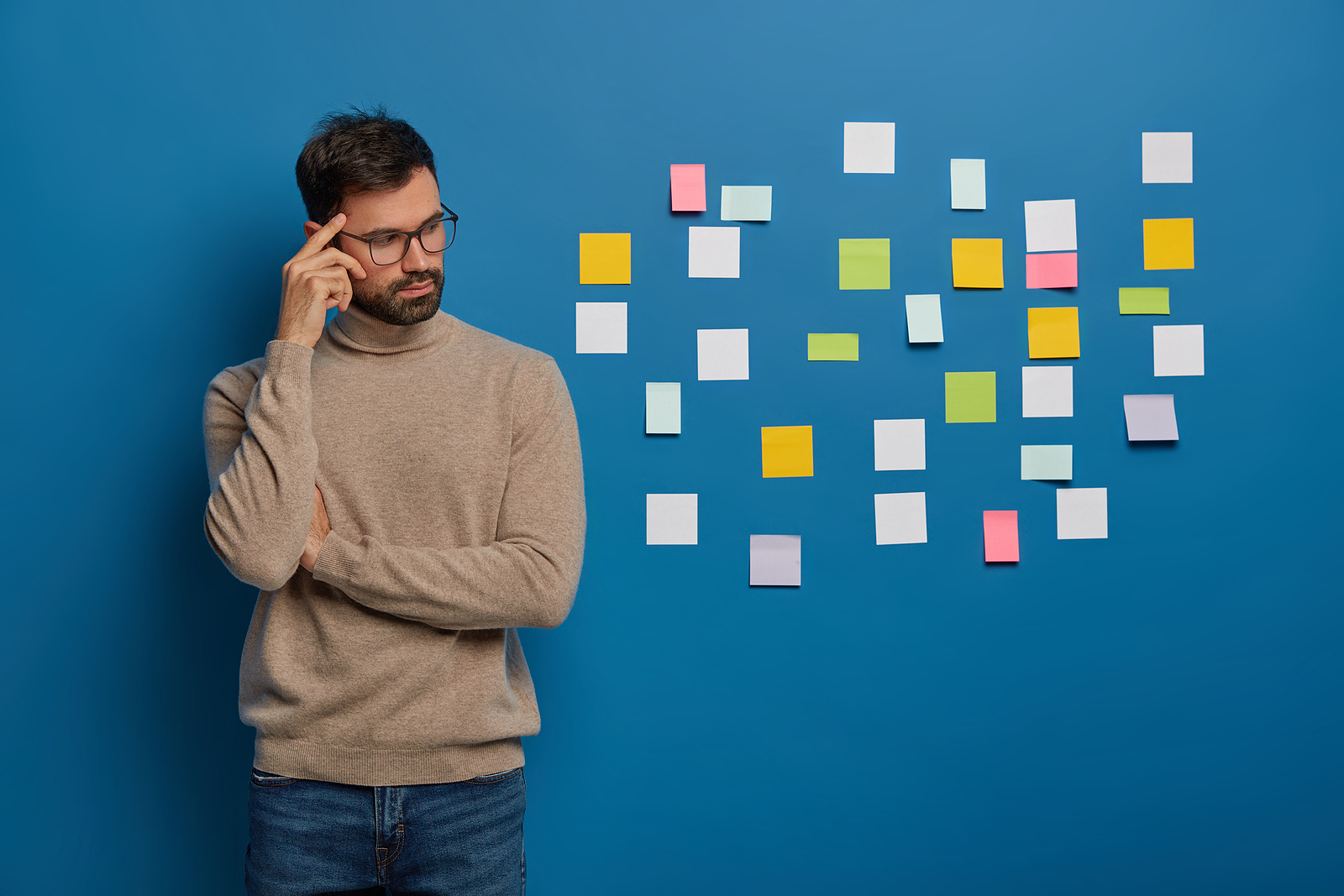 A man with glasses concentrates on something in front of a wall covered in sticknotes.