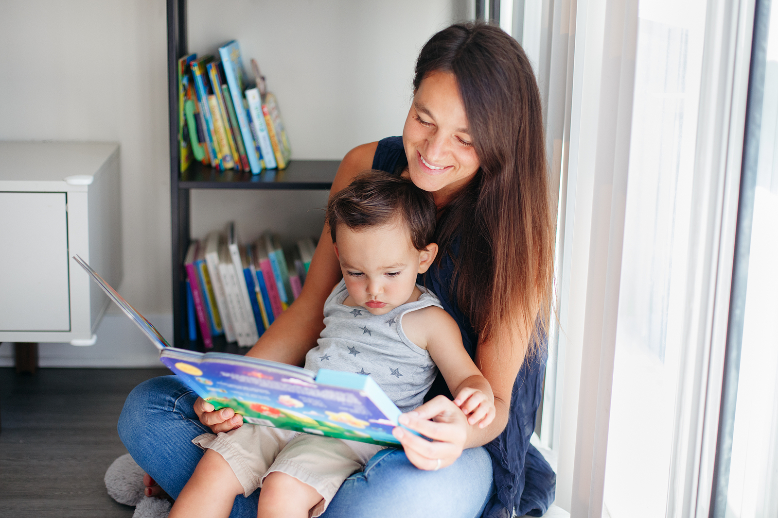 Mother with son boy sitting on floor at home and reading book together.