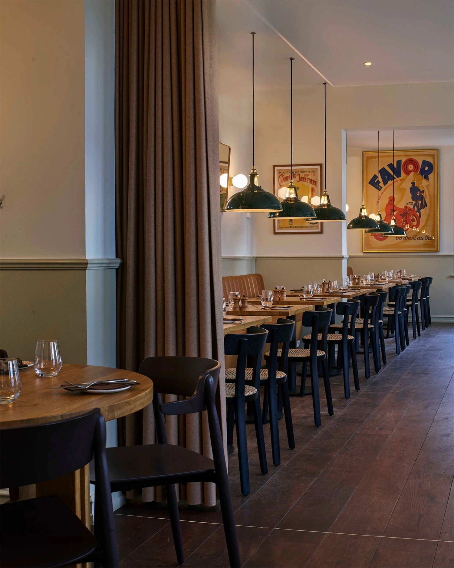 Looking down a Scandinavian restaurant at two rows of tables with Large Green Coolicon lampshades hanging above each one. 