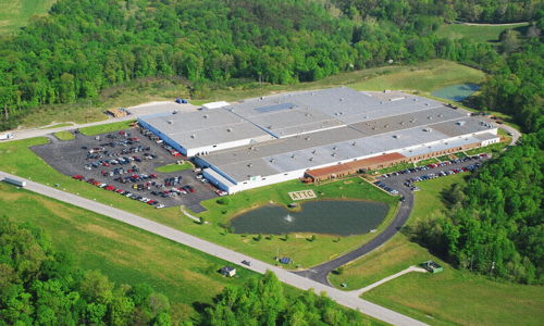 Aerial view of an industrial building amid greenery, with a tranquil pond and vibrant landscape, symbolizing harmony and productivity.