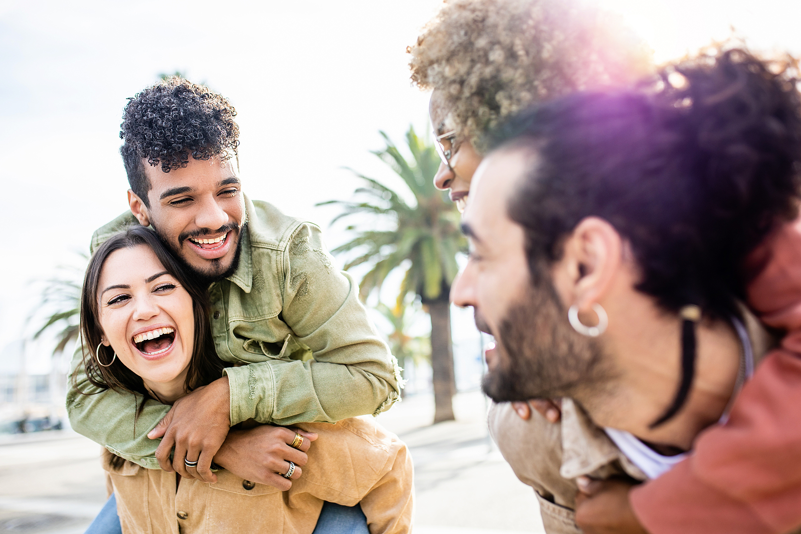 Two pairs of attractive couples laugh together while they carry their partners on their backs outdoors.