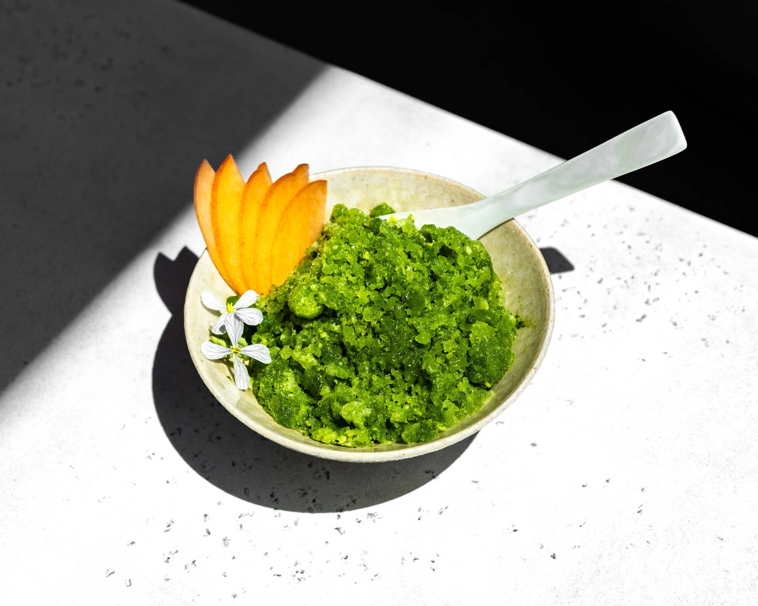  A bowl of bright green shaved ice, garnished with edible flowers and fruit.