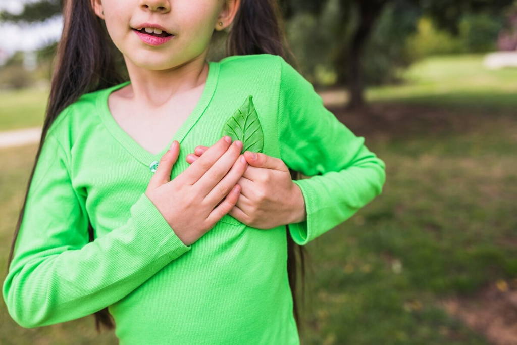 Jeune fille en chemise verte vif tenant une feuille contre sa poitrine dans un parc, symbolisant une connexion avec la nature.
