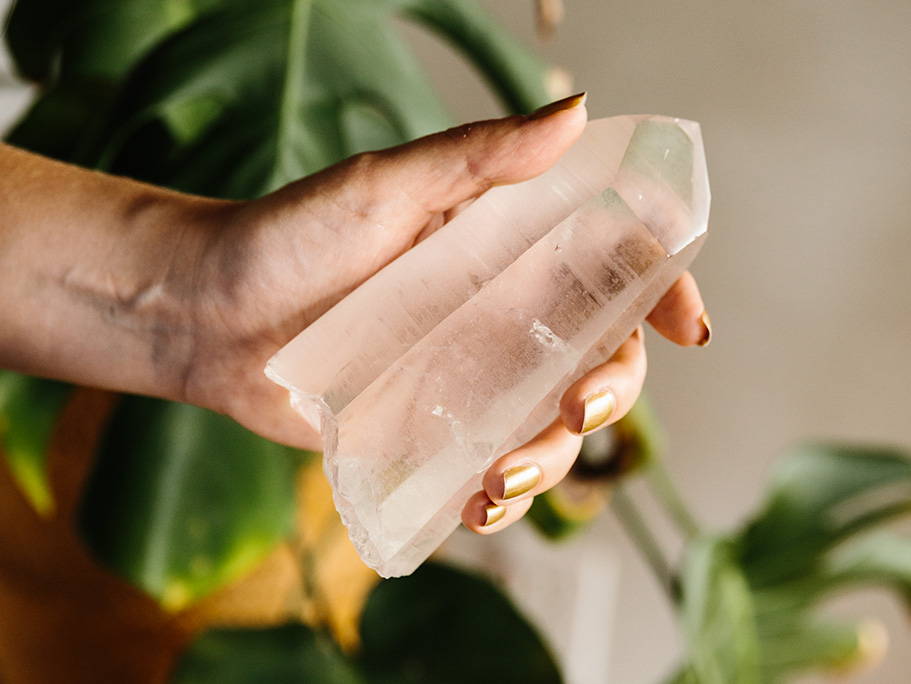 hand holding crystal point with indoor potted plant