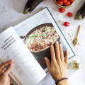 A person turns the page of a cookbook showing a recipe for Chicken and eggplant biryani