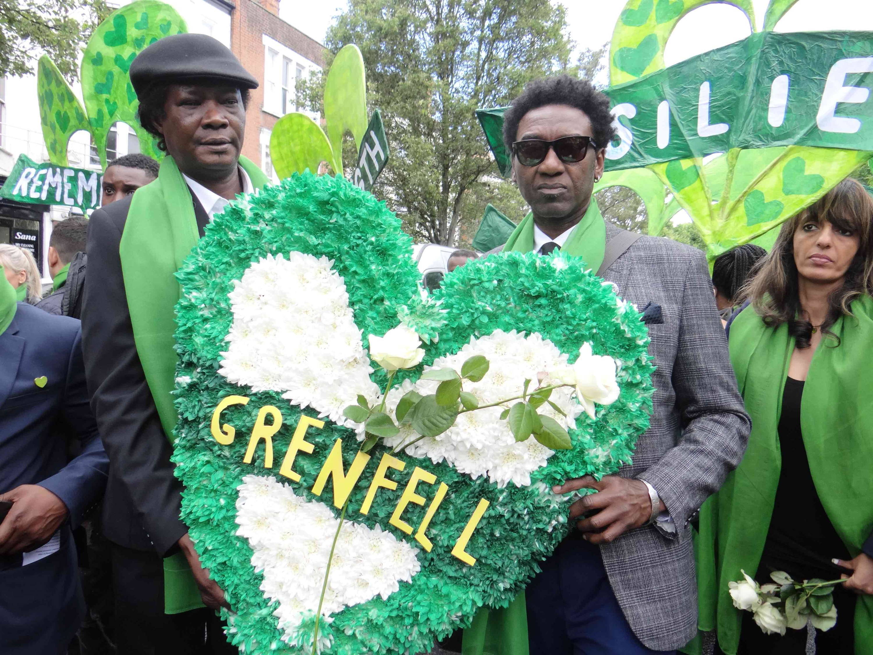 Two men holding a Grenfell floral tribute