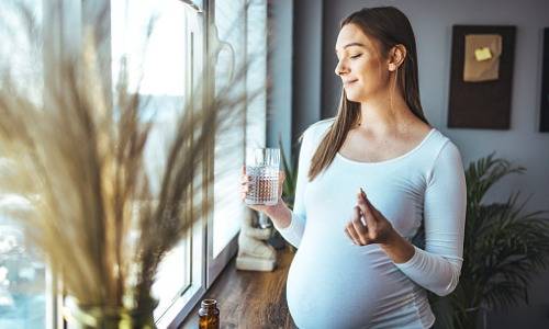 Schwangere mit Wasserglas und Kapsel in der Hand