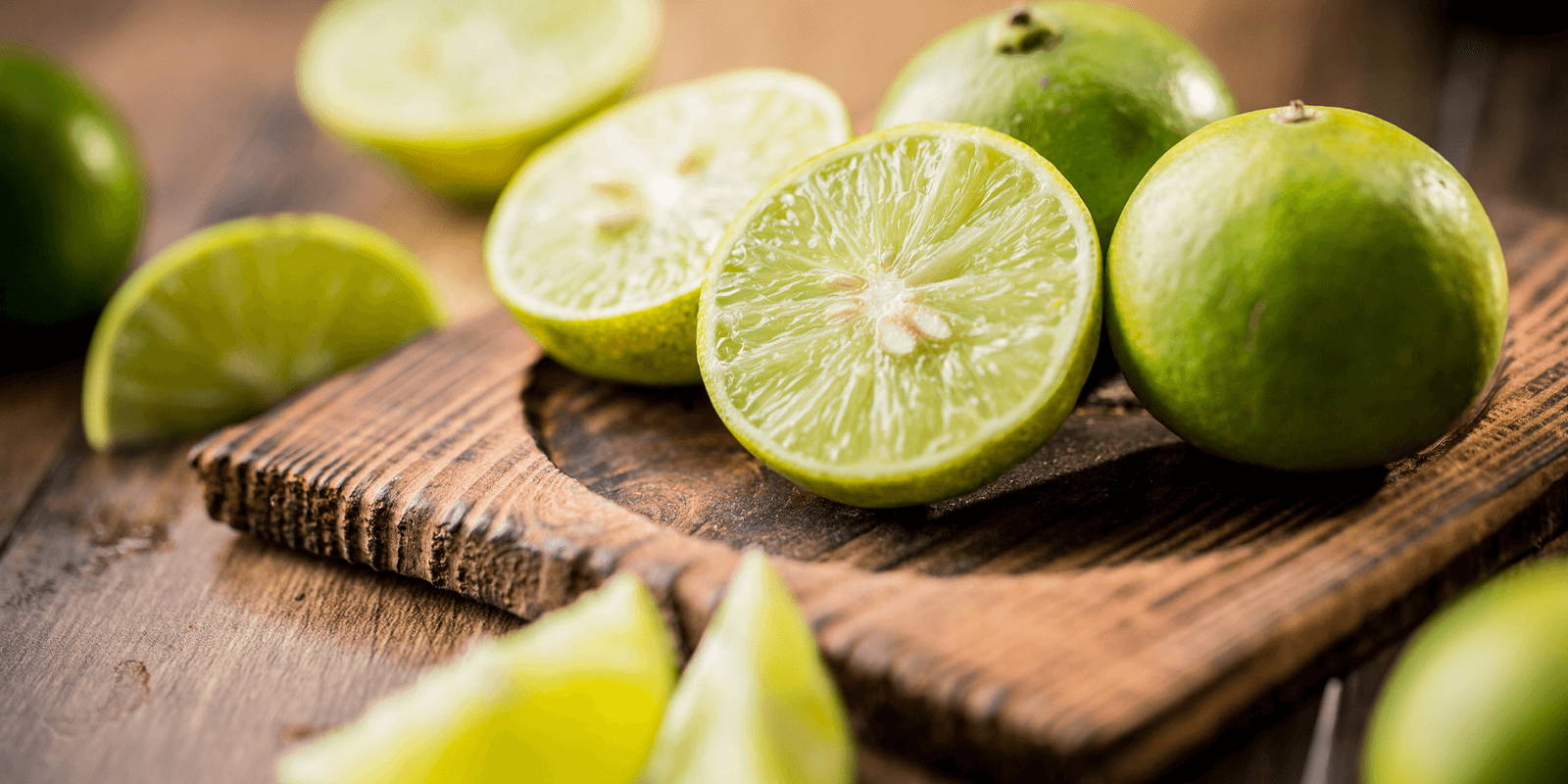 Whole, halved, and quartered limes scattered across a small wooden cutting board and wooden surface.