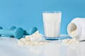 whey protein powder, glass of milk, and two dumbells on a blue background