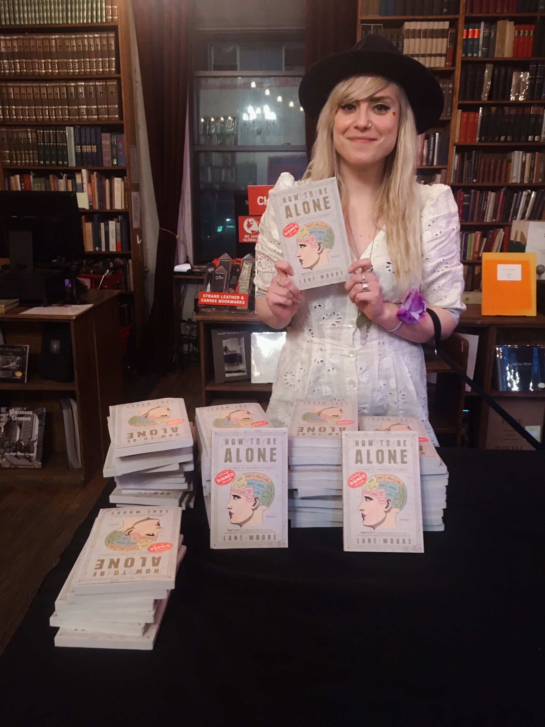 Lane Moore smiling and holding a copy of her book how to be alone during a booksigning event.