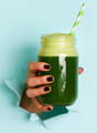 hand holding a mason jar of dark green wheat grass juice with a green and white striped straw