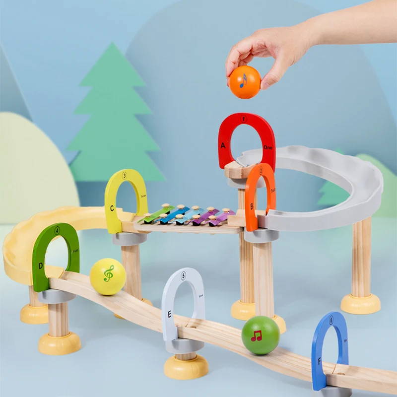 Un parcours musical en bois coloré InvenToy Montessori avec des arches multicolores et une main qui place une balle orange dessus. Certaines arches sont marquées de notes de musique et de lettres.