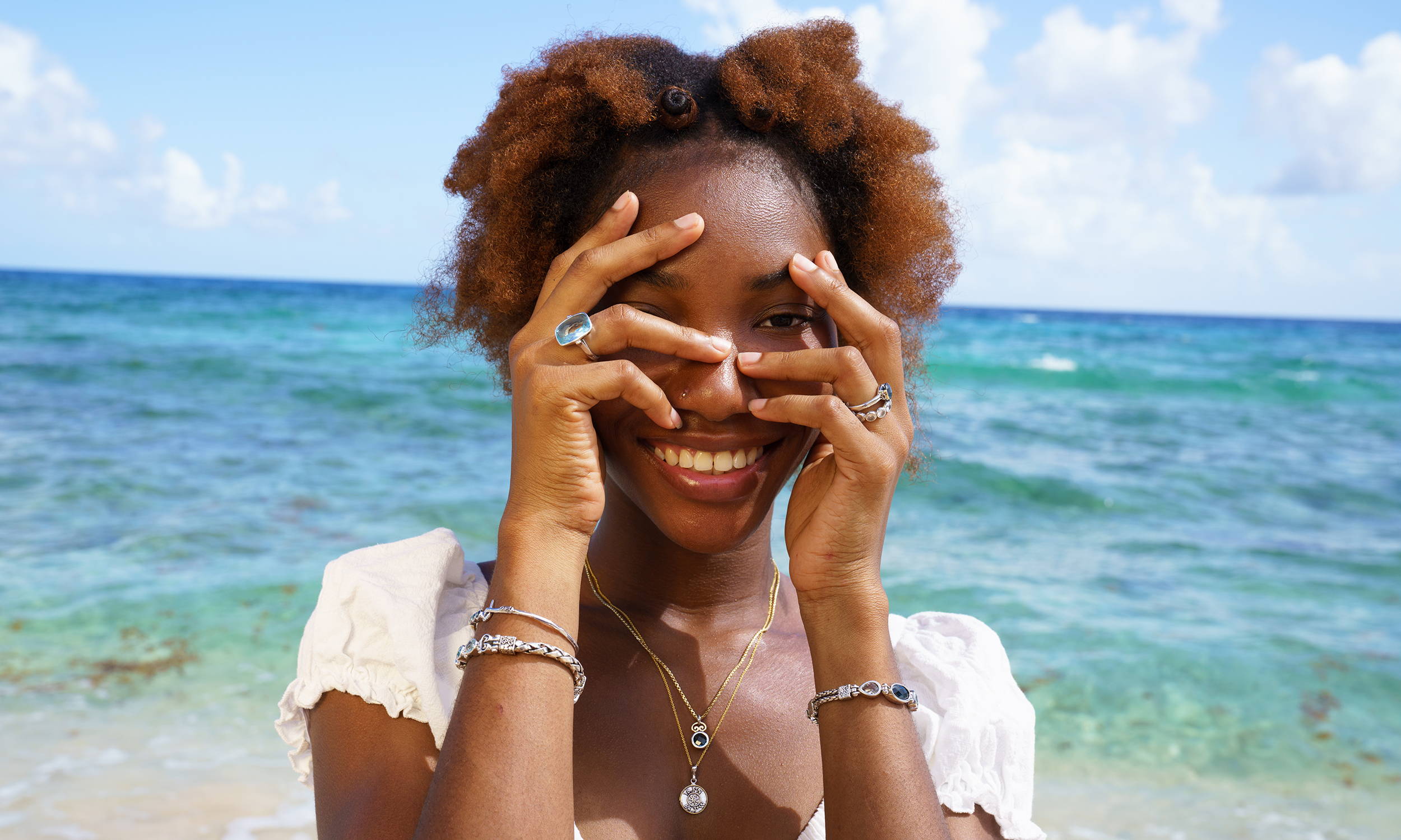 A young woman standing in front of the ocean showing off her jewelry style