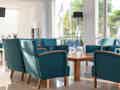 Ein einladender Loungebereich in der Lobby mit blauen Sesseln und Holztischen, beleuchtet durch große Fensterfronten.