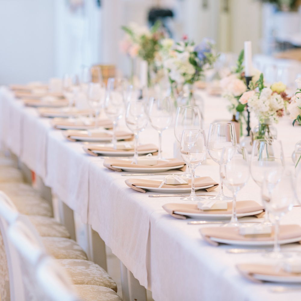 Long white banquet table set with plates & glasses