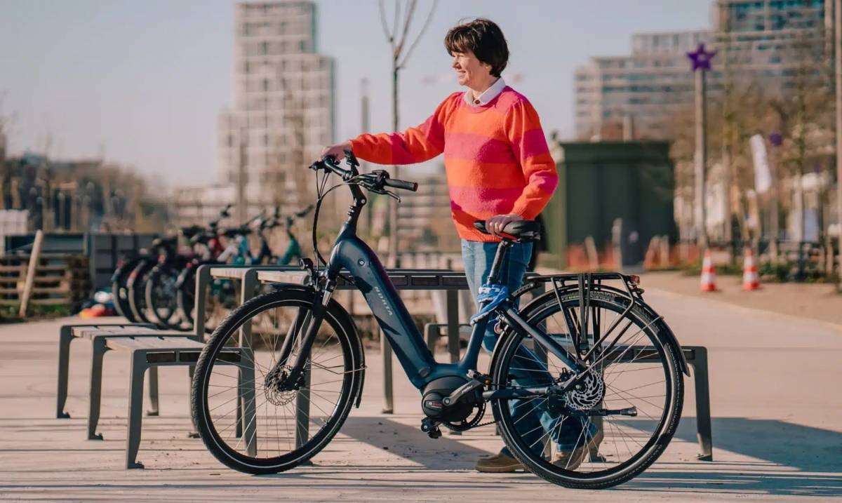 Femme souriante à côté de son vélo électrique de ville à cadre ouvert avec porte-bagages