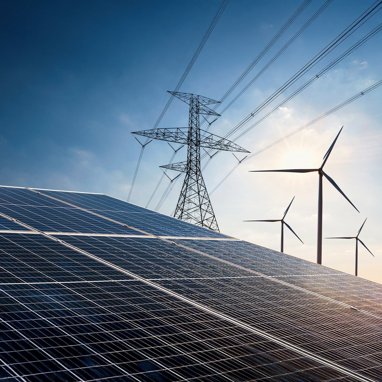 Close-up of solar panels in the foreground, with electricity pylons and wind turbines in the background against a blue sky, illustrating renewable energy sources and power transmission.