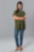 Woman crossing her arms while wearing a green high‐neck tunic top with short rolled sleeves, styled with fitted jeans and clear heels.