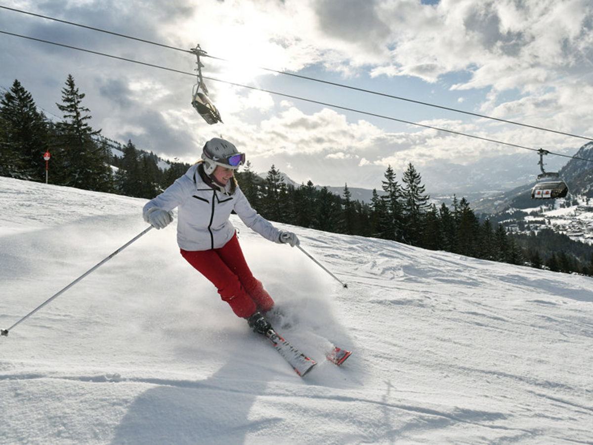 Skifahrerin fährt Kurve auf Piste. Schneelandschaft mit Gondelbahn im Hintergrund.