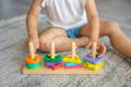 Toddler sitting on a rug and playing with a wooden Montessori-inspired colorful shape sorting toy.