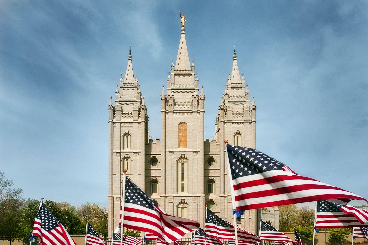 PHoto of hte Salt Lake City Temple with rows of US flags in the forefront.