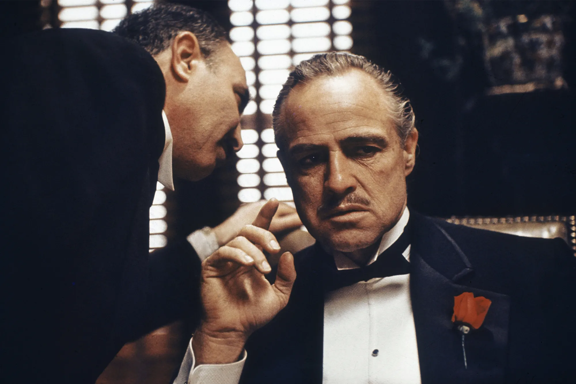 Marlon Brando as the Godfather, sitting and having one of his attendants whisper something into his ear.