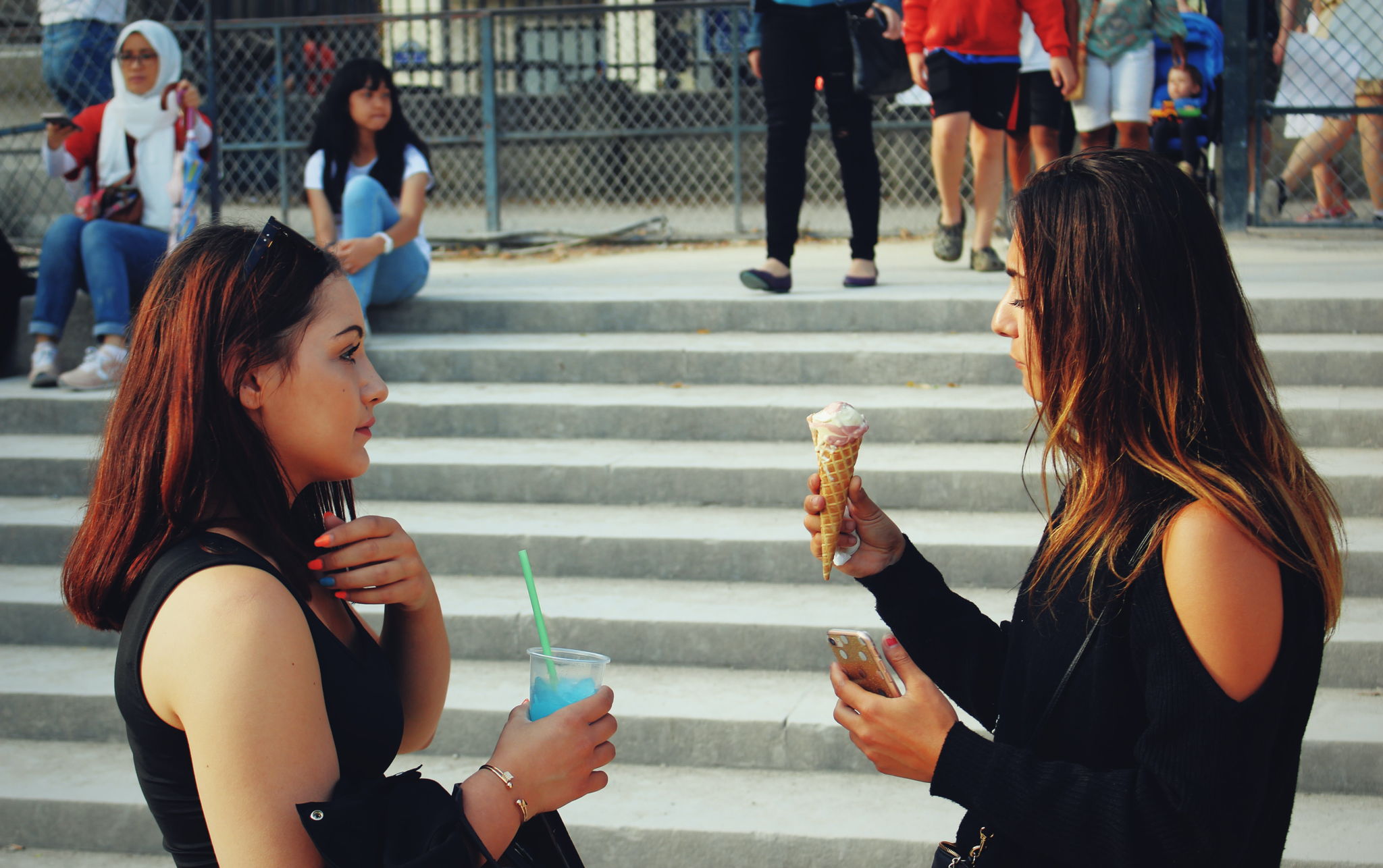Two girlfriends hanging out in front of stairs eating ice cream and talking.