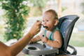 Little boy being fed while sitting in a kids lunch chair. 