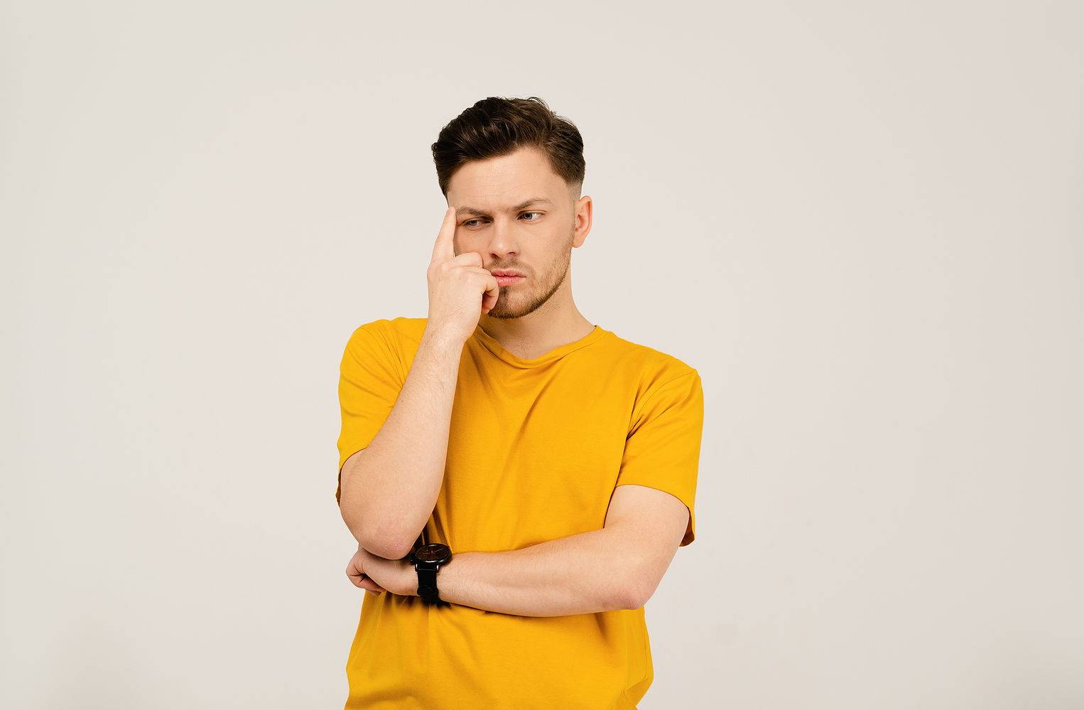 A young man folds his arms and looks pensive and concerned looking to the side.