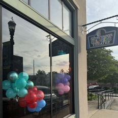 Storefront window adorned with colorful balloons, creating a joyful, festive atmosphere suggesting celebration and excitement.