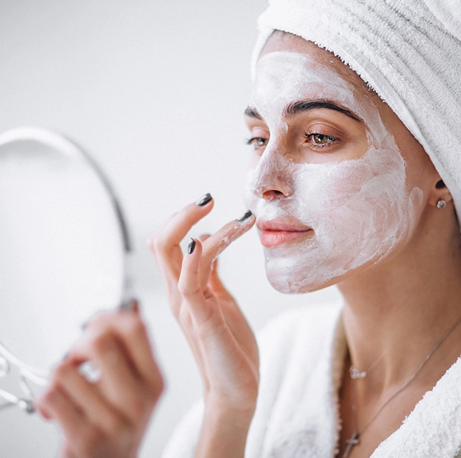 Une belle femme se regarde dans un miroir en appliquant une crème sur le visage.