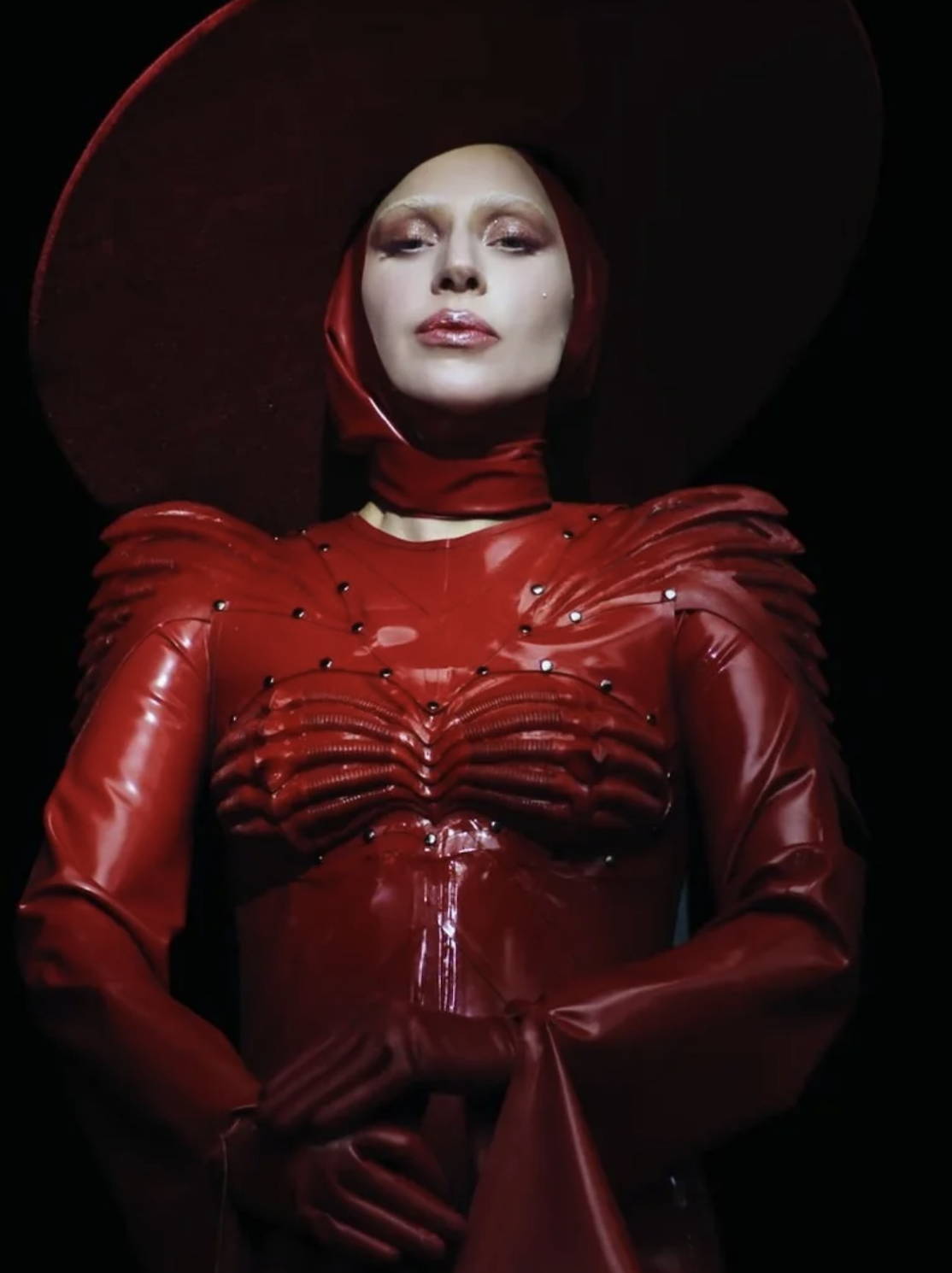 Lady Gaga in sculpted red latex gown with structured shoulders and matching wide-brim hat by Vex Clothing.