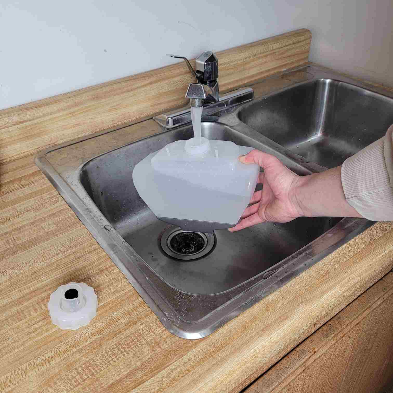 a photo of a person filling a steamer water tank under a tip in a sink