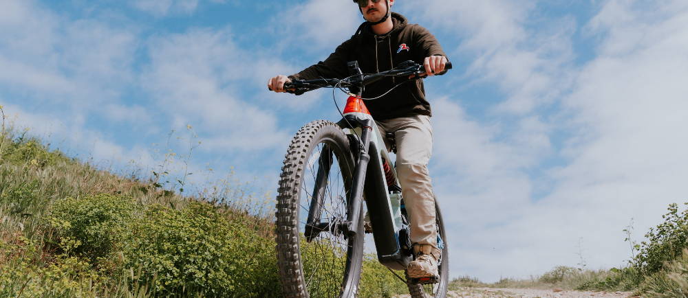 a man riding a Cannondale Moterra Neo Worth on a bike path surrounded by grass in front of the ocean