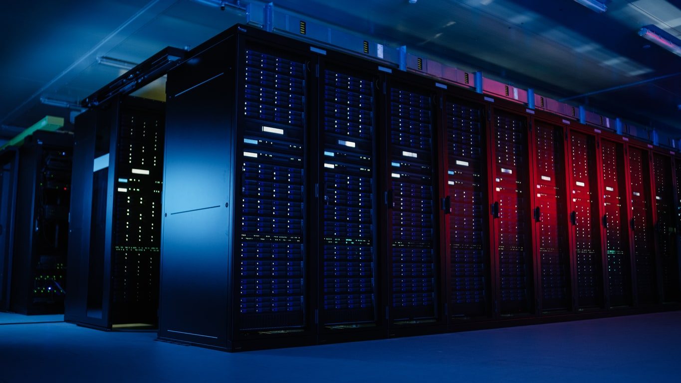 A row of black server racks with blue and red LED lights in a modern data center, illuminated by cool and colored lighting.