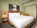 Modernes Hotelzimmer mit Kingsize-Bett, senfgelbem Sessel und stilvoller Schwarz-Weiß-Kunst über dem Bett.