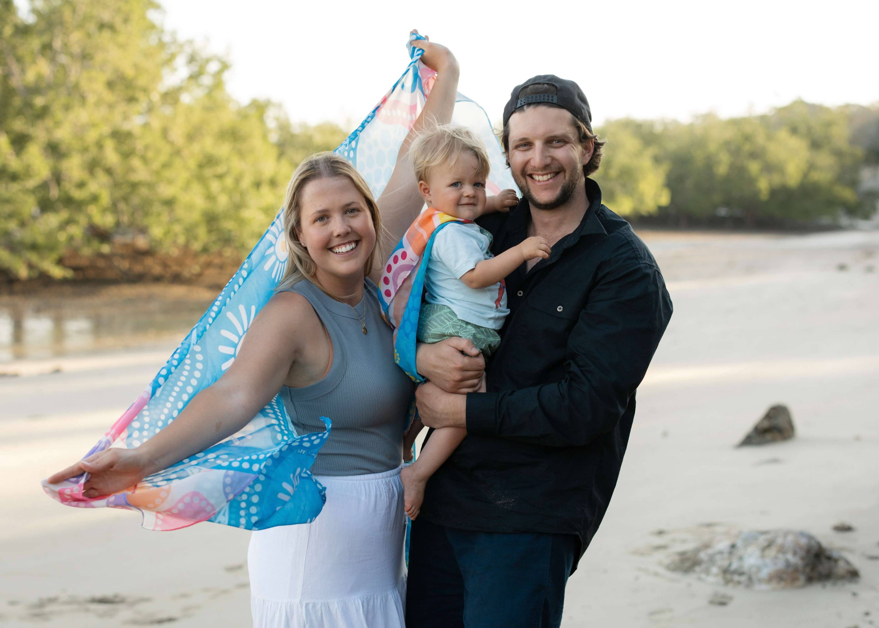 Caitlin holding a scarf with her artwork next to her husband and baby