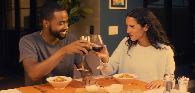 Young couple toasting glasses of red wine at home with bowls of elegant ZENB Pasta dishes.