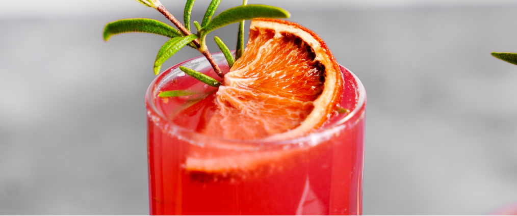 a glass of a red Mimosa Mocktail with a slice of orange