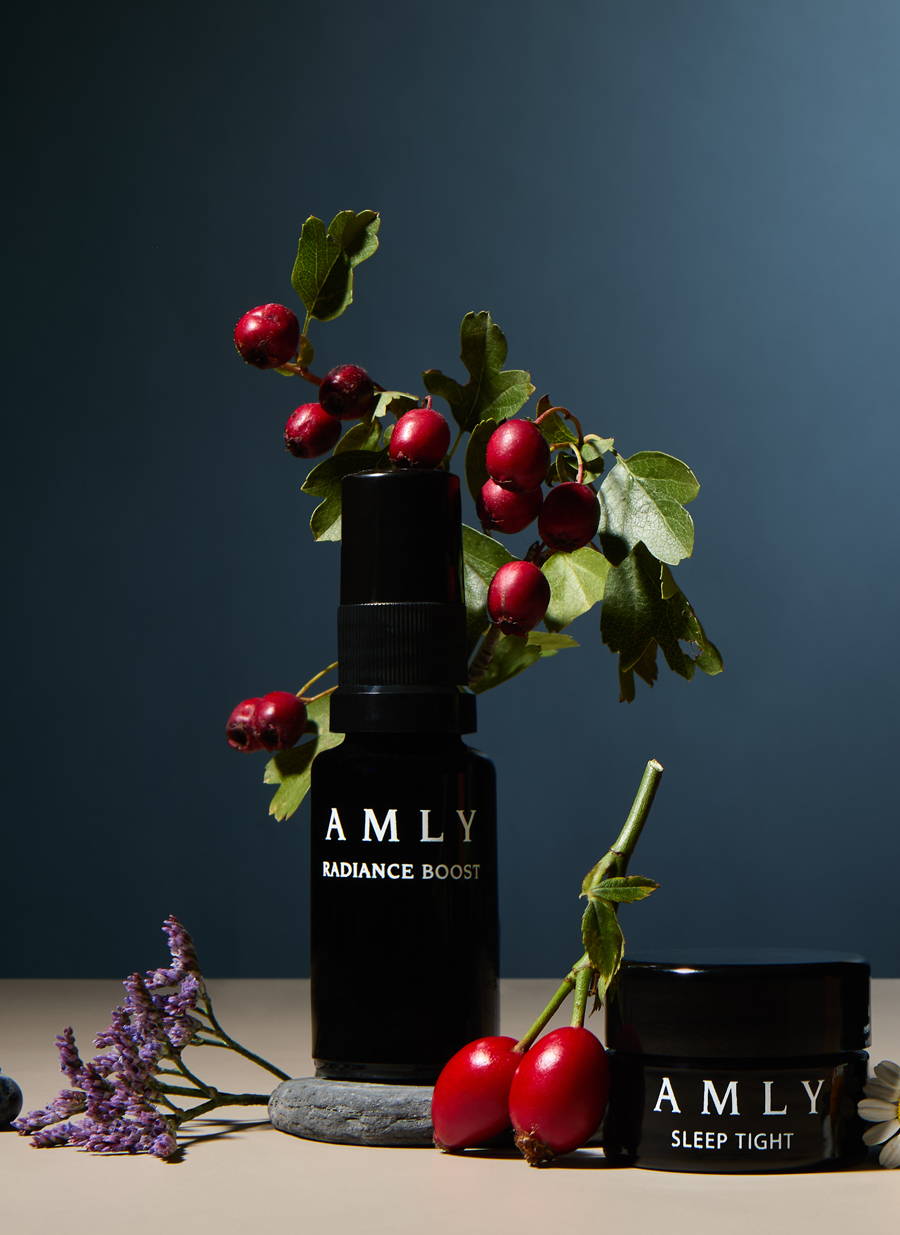 AMLY products surrounded by berries and flowers with a dark blue background