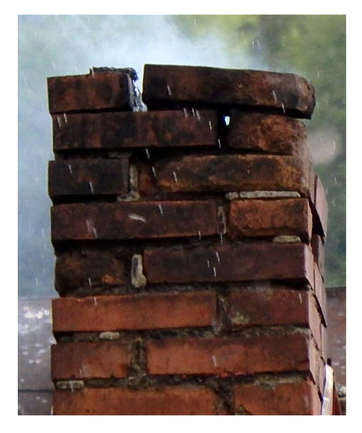 A deteriorating brick chimney with missing bricks and visible rain exposure.