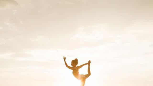 Silhouette of a person doing a standing split pose against a bright sky at sunset or sunrise.