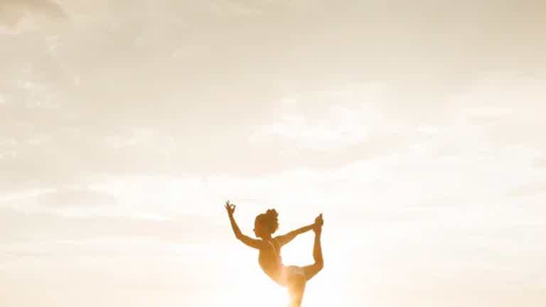 Silhouette of a person doing a standing split pose against a bright sky at sunset or sunrise.